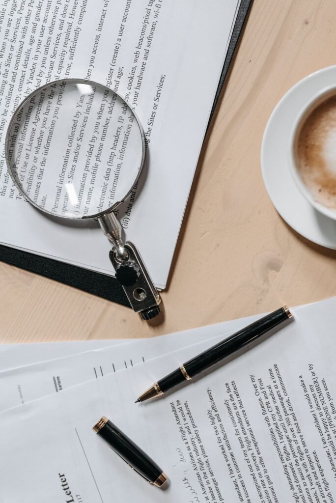 A magnifying glass resting over the fine print of a document beside a pen
