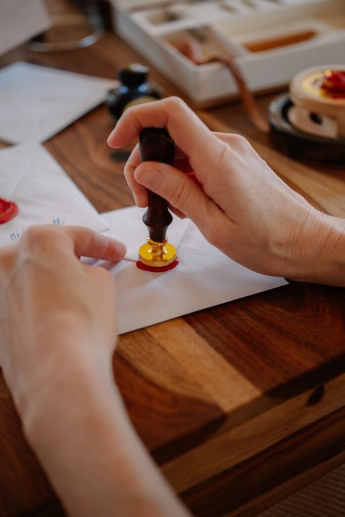 A hand pressing a seal onto a sealed envelope on a wooden table